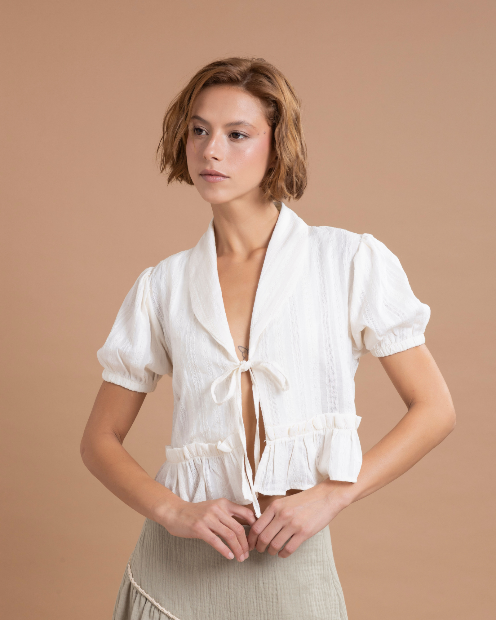 Blusa insignia de la marca, con mangas globo y bolero en la parte inferior que aportan volumen y movimiento. En el frente, cuenta con tiras para anudar en un moño, creando un detalle femenino y elegante.