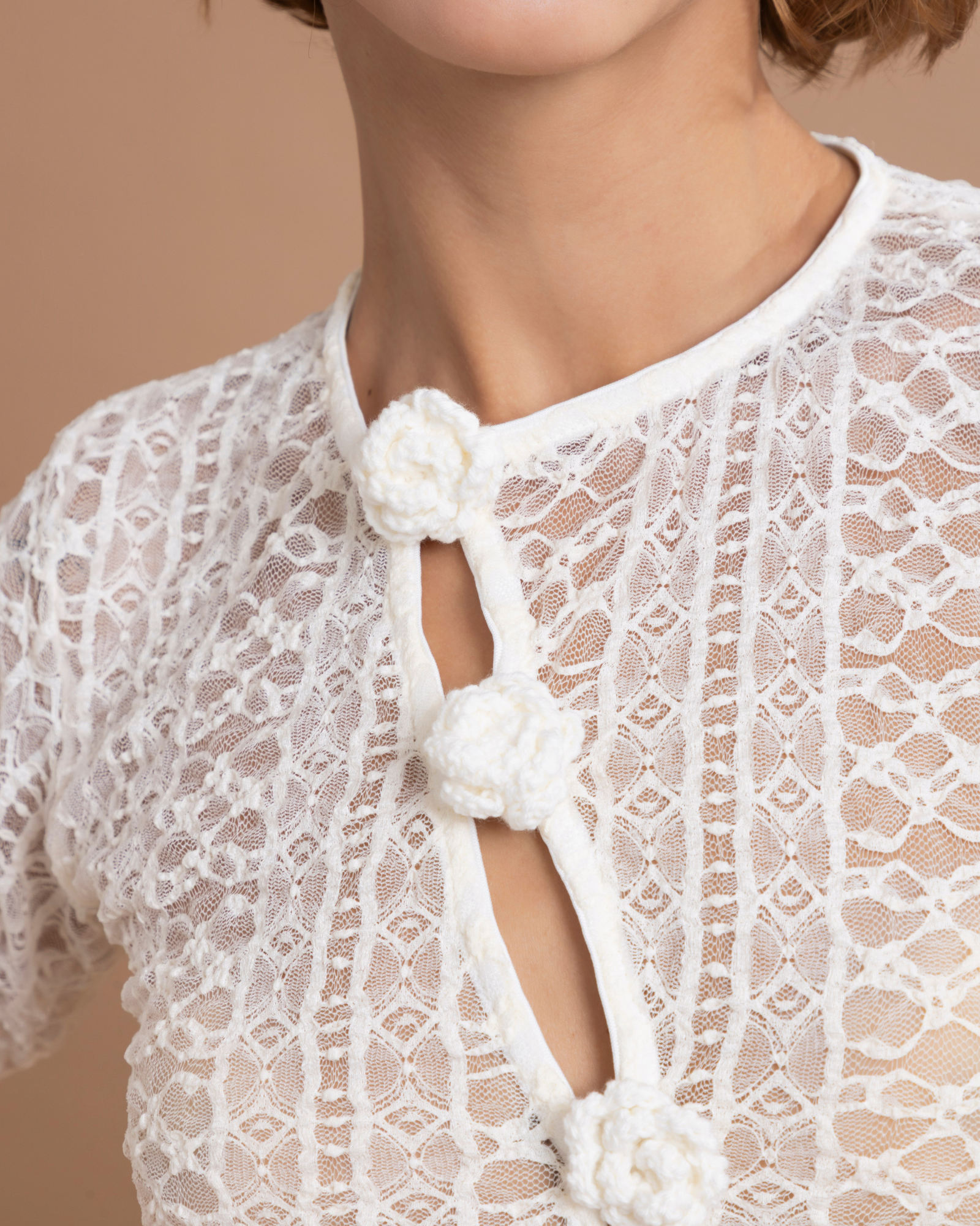 Buzo confeccionado en blonda, con abertura asimétrica en la parte delantera. Los botones están tejidos a mano en técnica crochet. La tela elástica permite que la prenda, de talla única, se ajuste a diferentes talas, desde la S hasta la L.