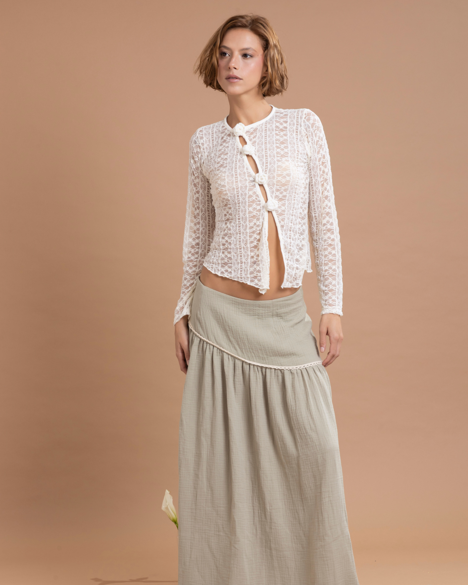 Buzo confeccionado en blonda, con abertura asimétrica en la parte delantera. Los botones están tejidos a mano en técnica crochet. La tela elástica permite que la prenda, de talla única, se ajuste a diferentes talas, desde la S hasta la L.