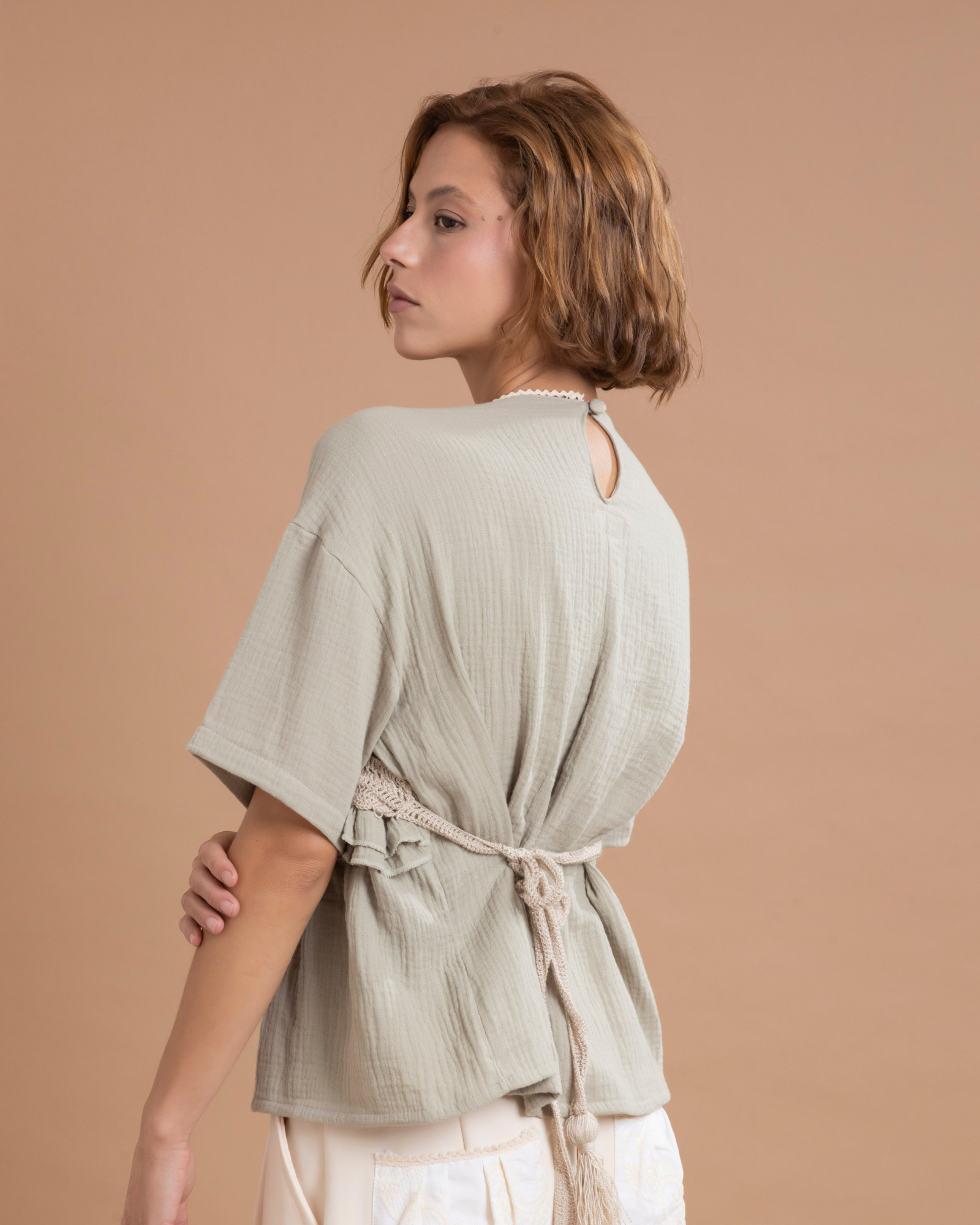 Camisa estilo t-shirt confeccionada en algodón, con un aplique en forma de top elaborado en técnica crochet, 100% tejido a mano. Presenta boleros decorativos a la altura de la cintura y tiras posteriores que salen desde los costados, permitiendo ajustarla y anudarla con un moño en la parte trasera.