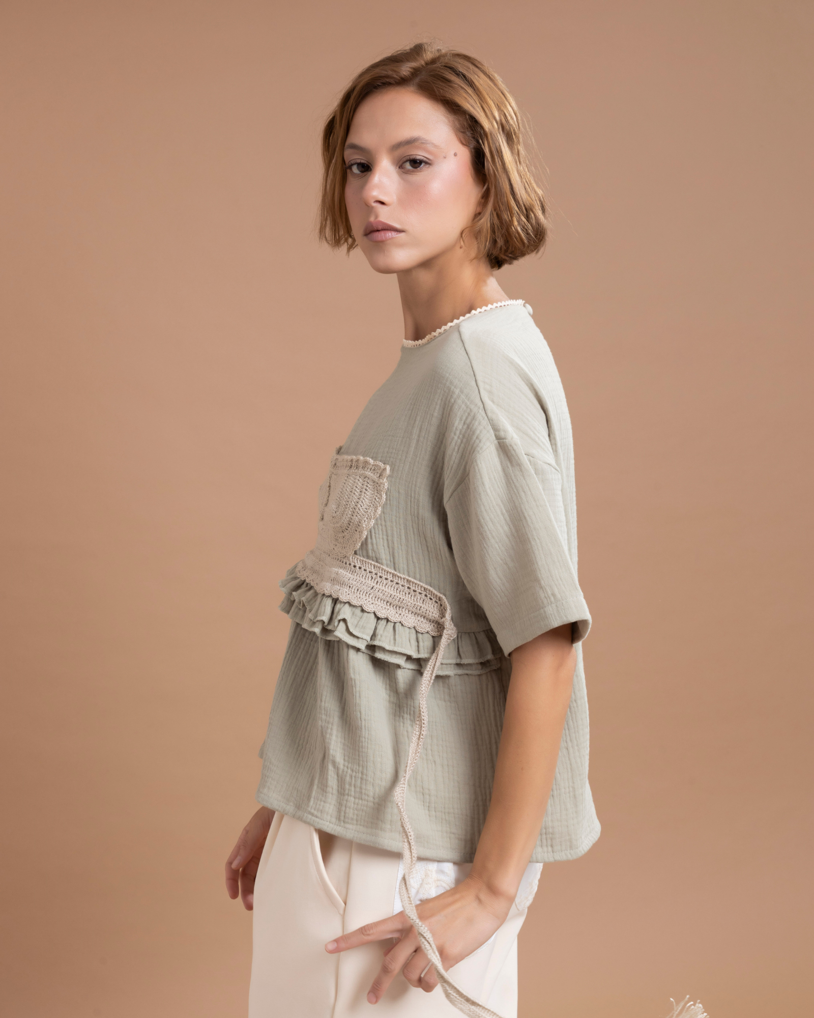 Camisa estilo t-shirt confeccionada en algodón, con un aplique en forma de top elaborado en técnica crochet, 100% tejido a mano. Presenta boleros decorativos a la altura de la cintura y tiras posteriores que salen desde los costados, permitiendo ajustarla y anudarla con un moño en la parte trasera.