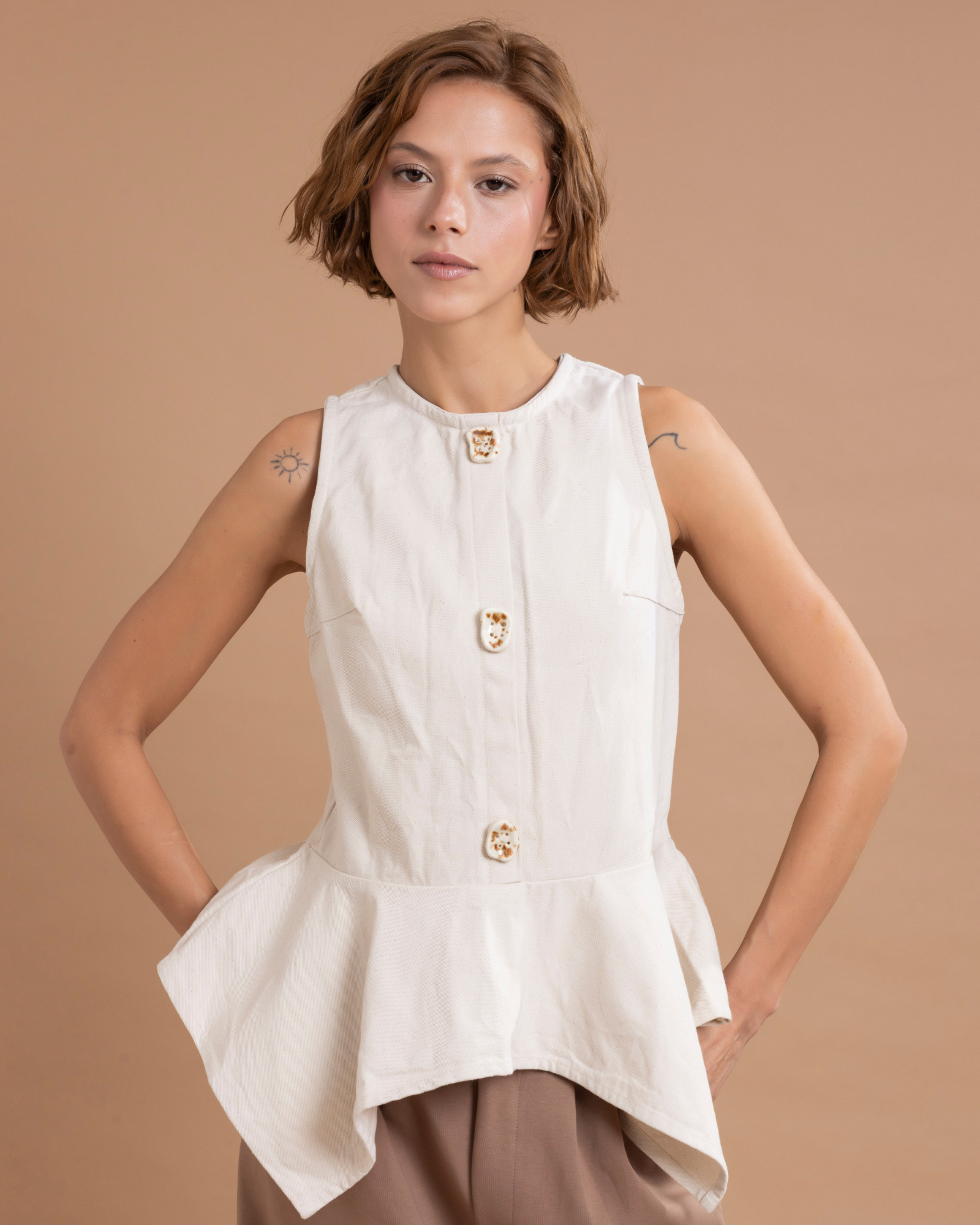 Prenda confeccionada en dril, ajustada al cuerpo y con peplum en la parte inferior que aporta volumen y elegancia. Sus botones de cerámica, 100% hechos a mano, son decorativos, y un cierre posterior asegura un ajuste perfecto.