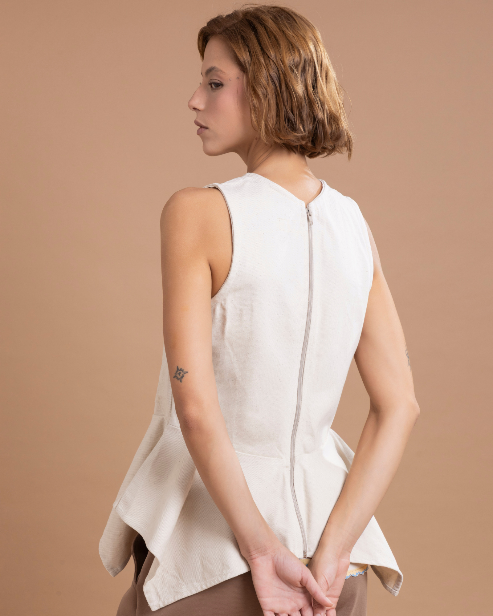 Prenda confeccionada en dril, ajustada al cuerpo y con peplum en la parte inferior que aporta volumen y elegancia. Sus botones de cerámica, 100% hechos a mano, son decorativos, y un cierre posterior asegura un ajuste perfecto.