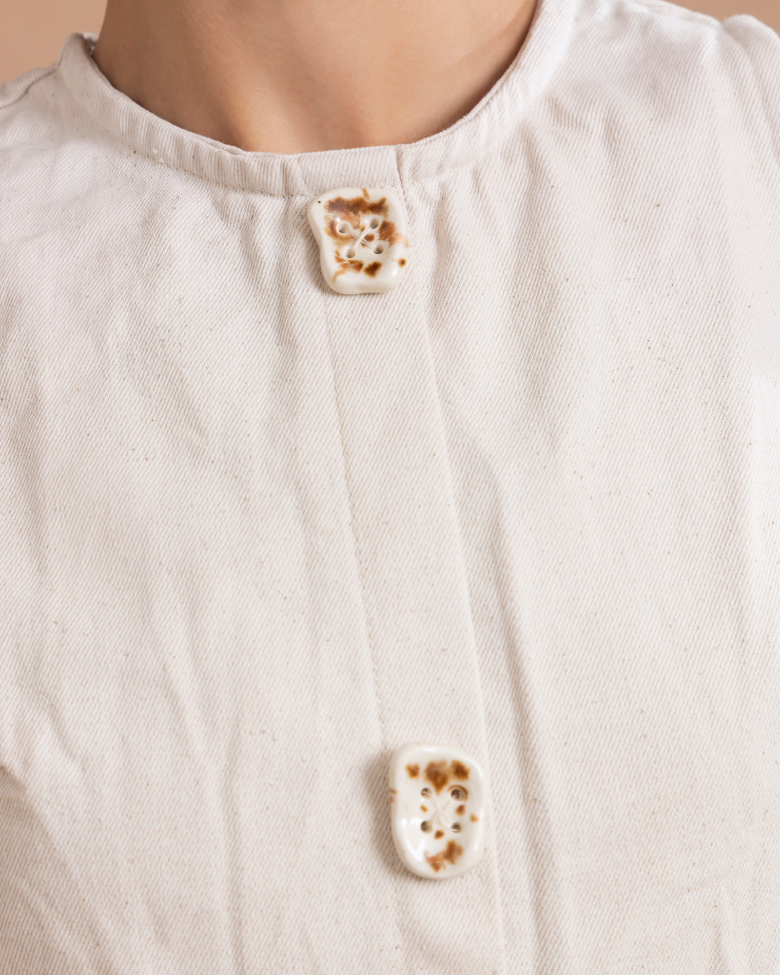 Prenda confeccionada en dril, ajustada al cuerpo y con peplum en la parte inferior que aporta volumen y elegancia. Sus botones de cerámica, 100% hechos a mano, son decorativos, y un cierre posterior asegura un ajuste perfecto.