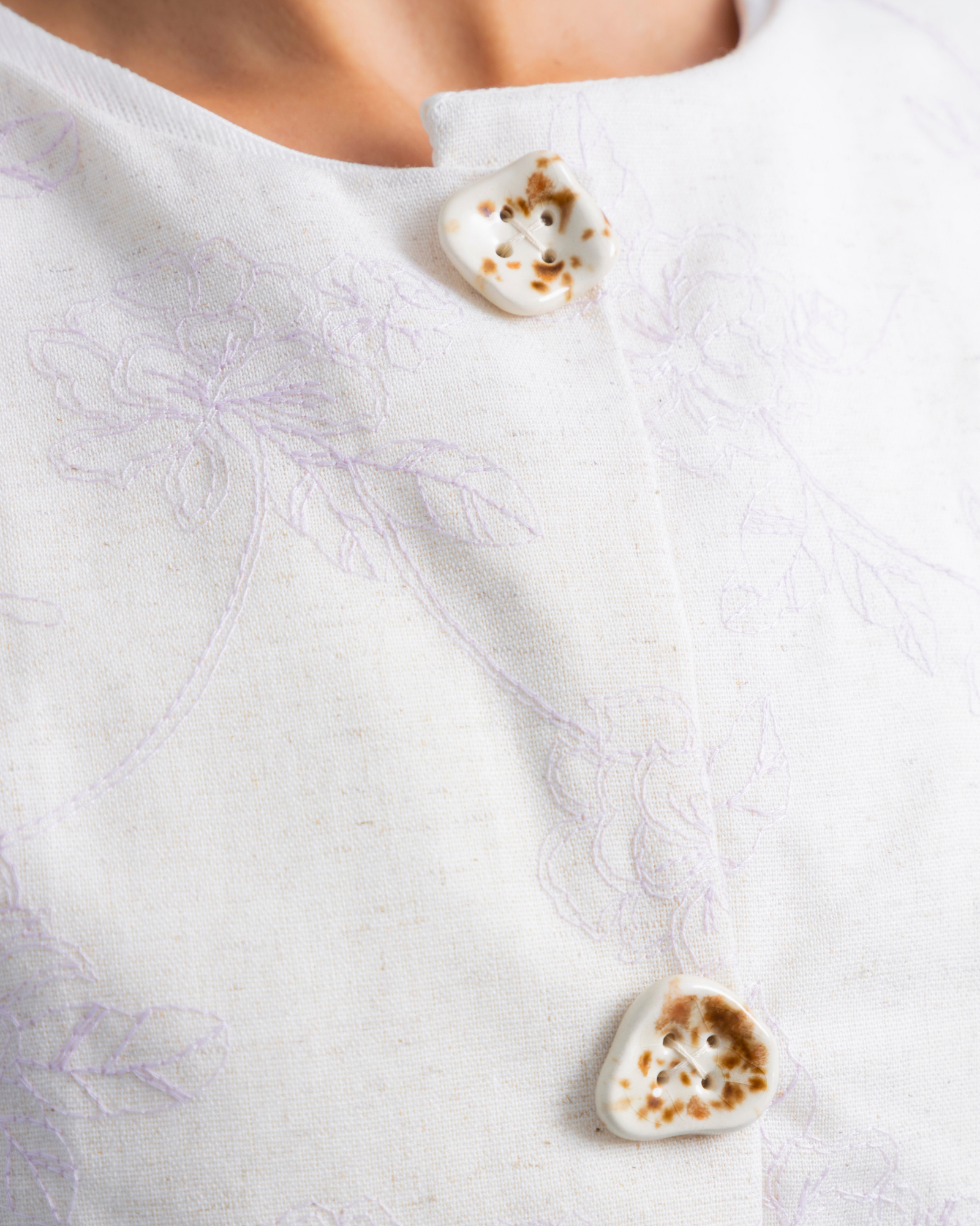 Chaleco tipo peto confeccionado en lino con textura de bordado, de estilo asimétrico. En el frente, botones decorativos de cerámica 100% hechos a mano.