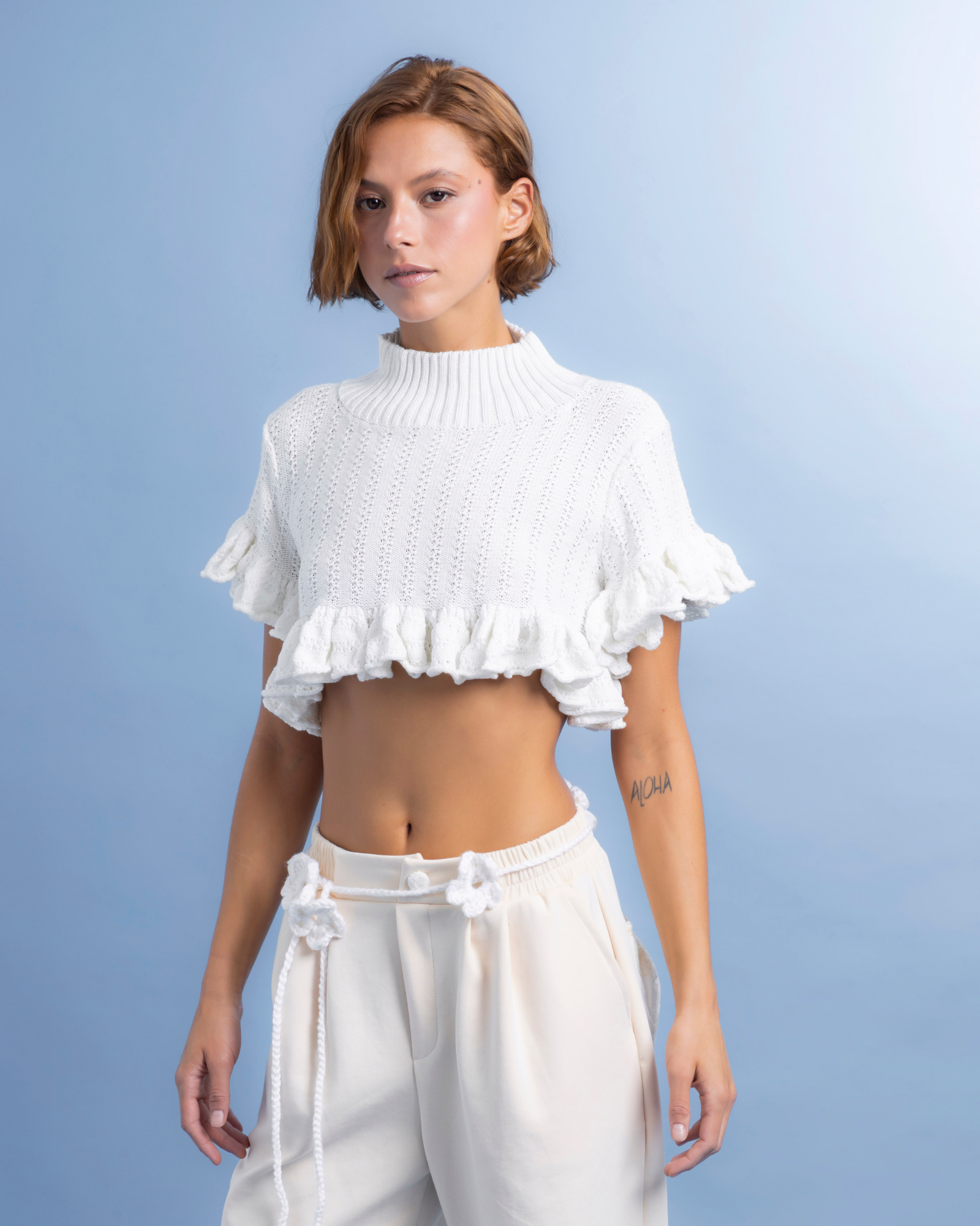 Prenda tejida en algodón, de cuello alto y corte corto, ideal para usar como crop top o como sobrepuesto. La parte inferior cuenta con boleros que aportan movimiento y un detalle femenino.